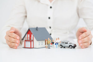 Image of a woman with a model of a family in front of a model house and car to illustrate the benefits of income protection insurance from Cathedral Independent Planning Ltd